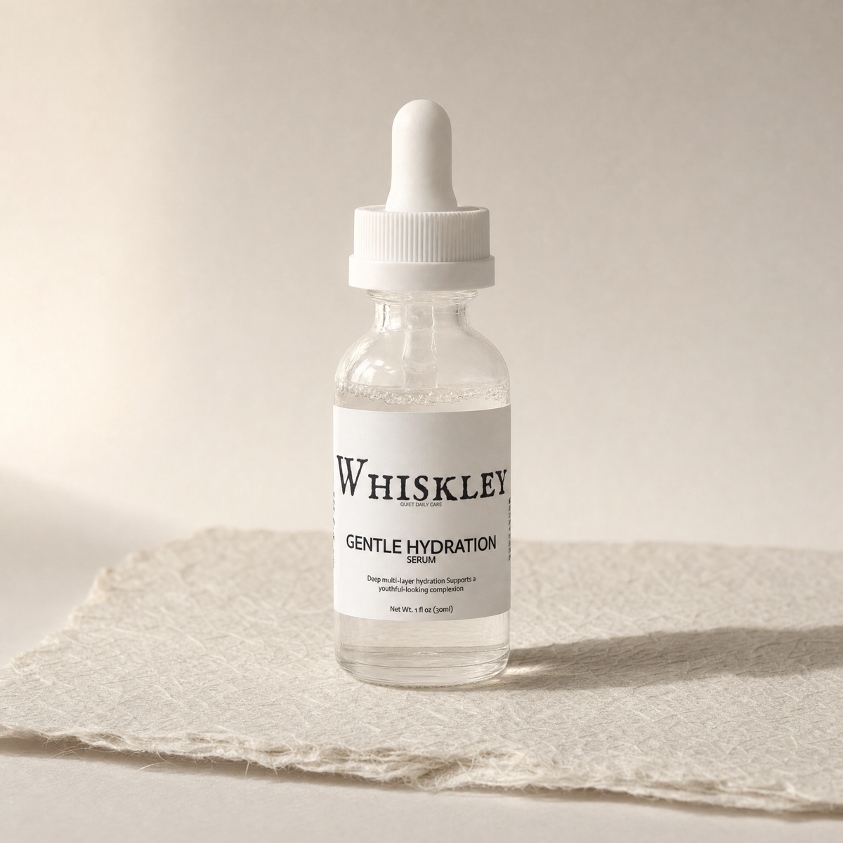 Whiskley Gentle Hydration Serum clear glass dropper bottle with white dropper cap standing on textured washi paper under warm side light